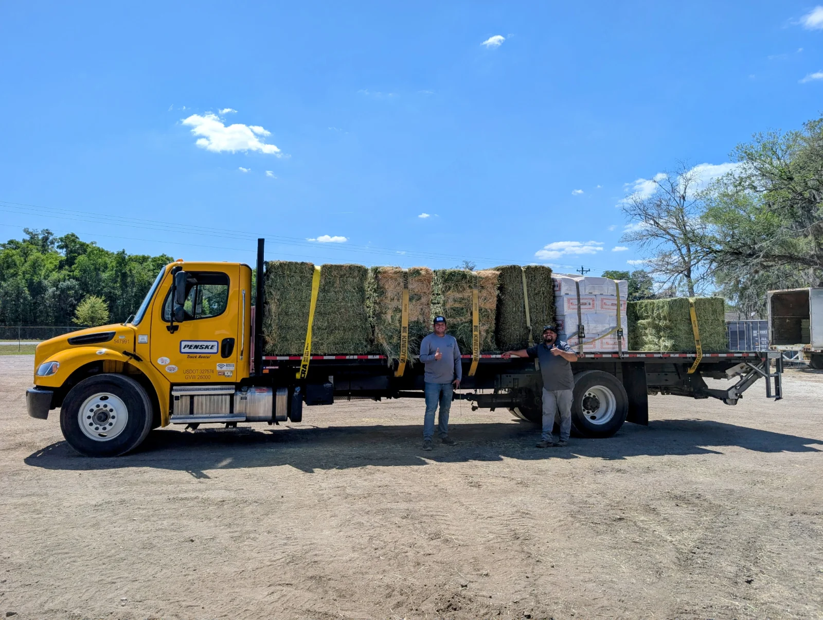 Team loading hay bales onto customer truck with forklift